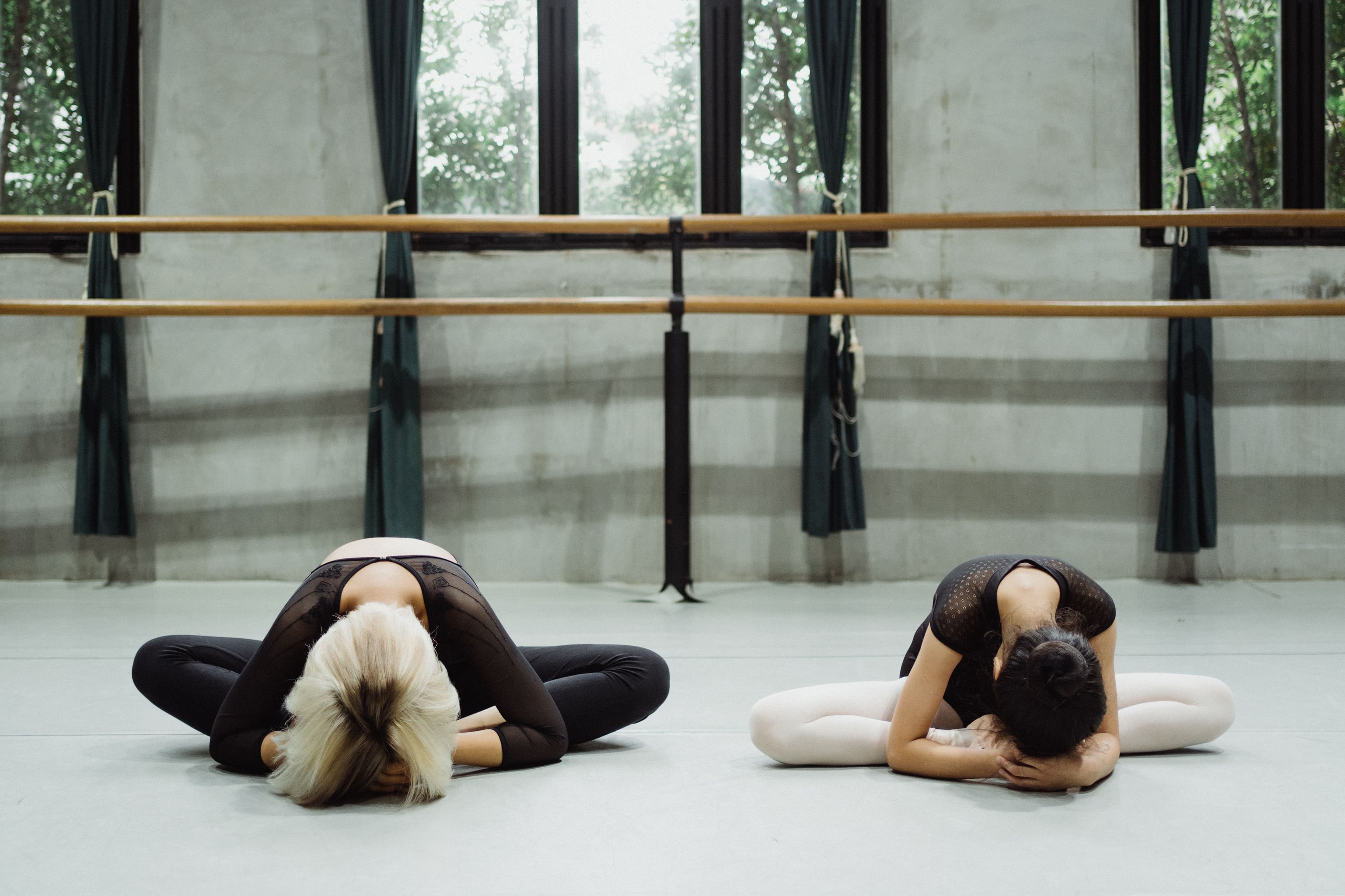 An instructor guides a student through a stretch at the barre in a daylit studio